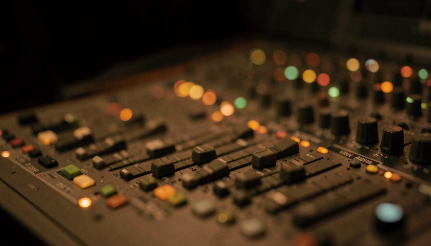 Close-up of a broadcast mixing console with warm brown and olive-green faders glowing softly in a dim studio
