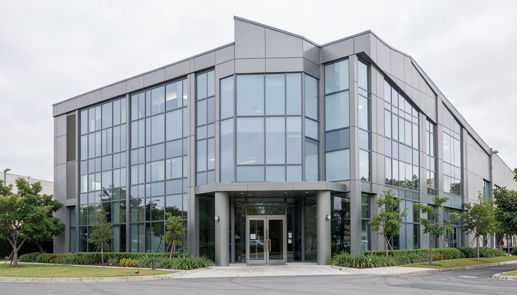 A clean, modern office building exterior in muted gray and glass tones, set against a soft overcast sky with subtle green landscaping